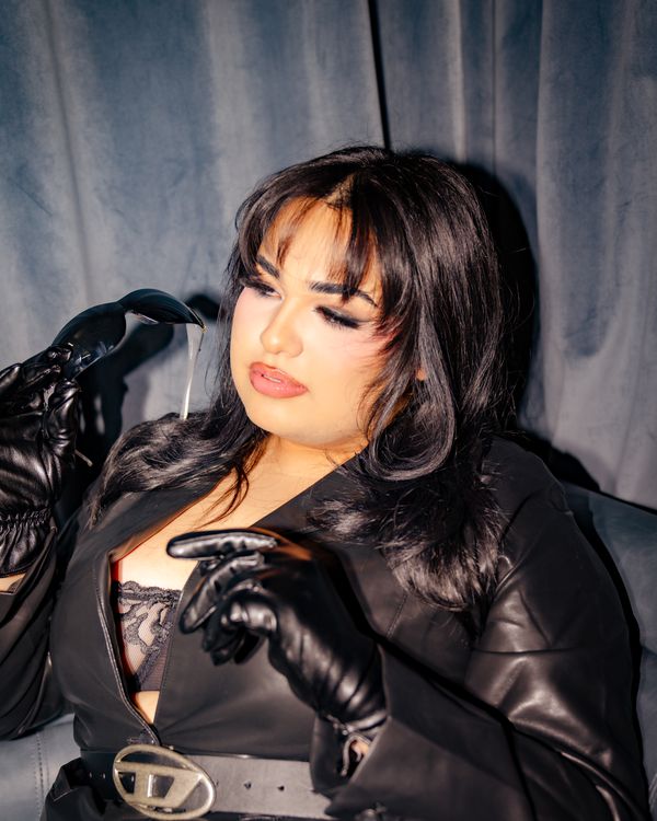 Model in a black leather coat and gloves against a blue velvet curtain