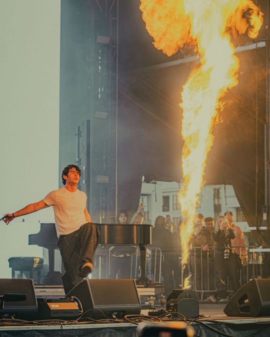 Performer on a festival stage with a column of fire behind a piano