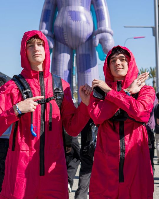 Two festival-goers in red hooded jumpsuits in front of a giant inflatable