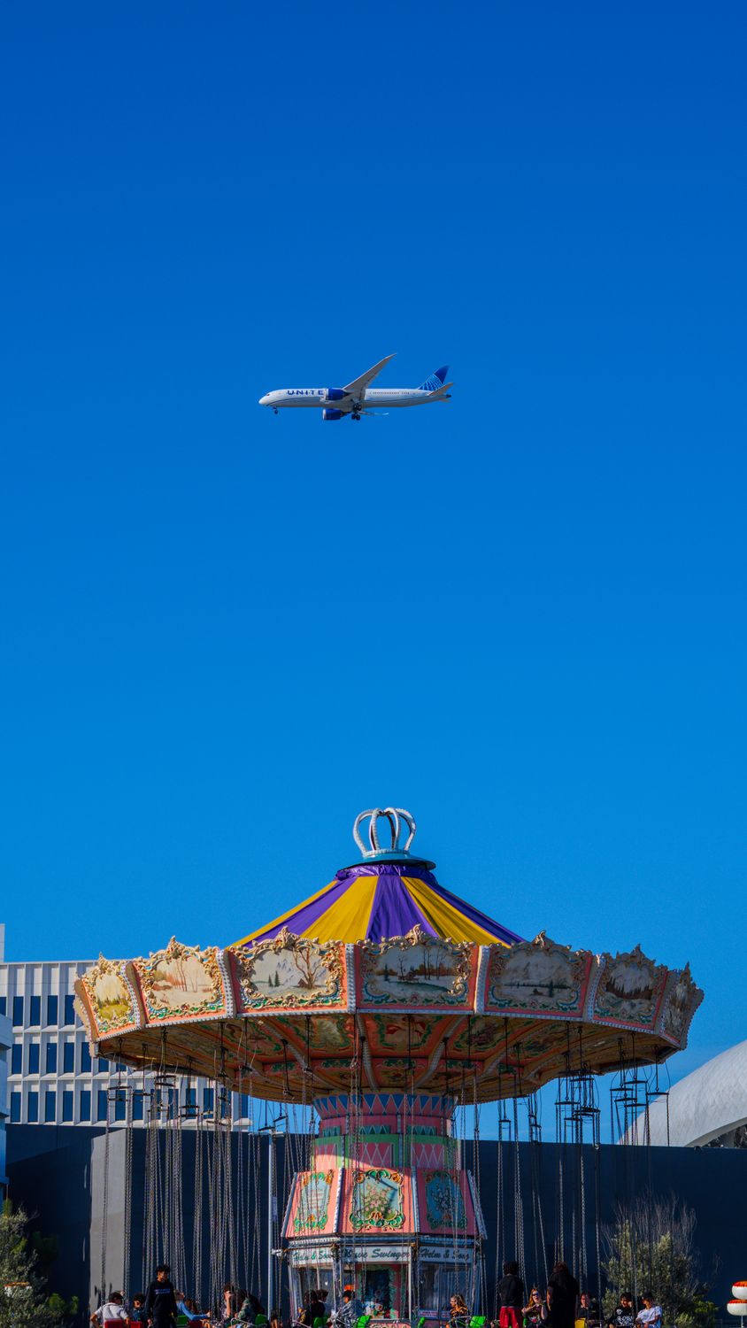 An airliner crossing a deep blue sky above a festival carousel