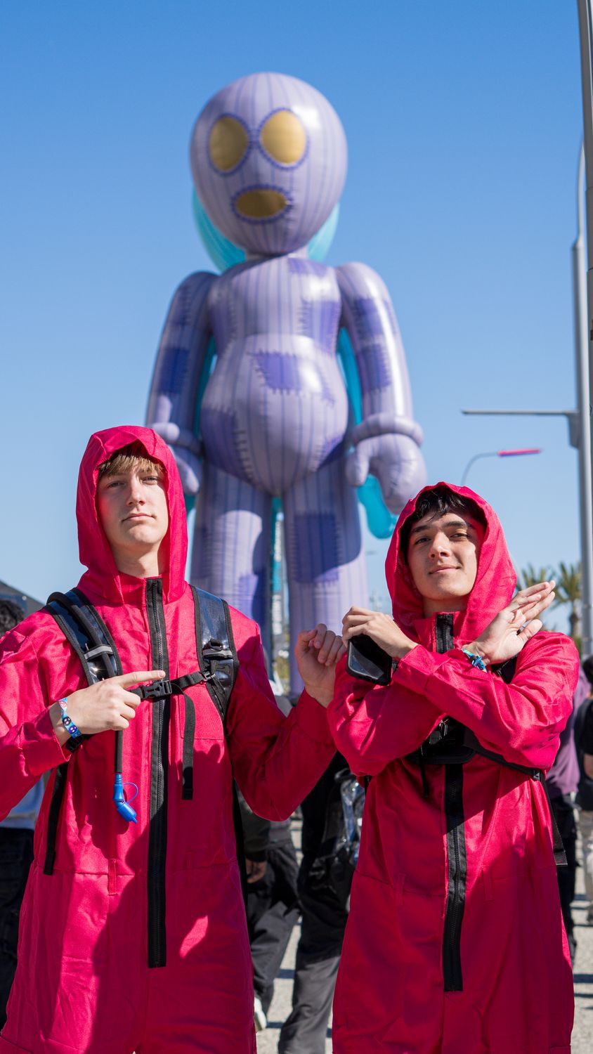 Two festival-goers in red hooded jumpsuits in front of a giant inflatable character
