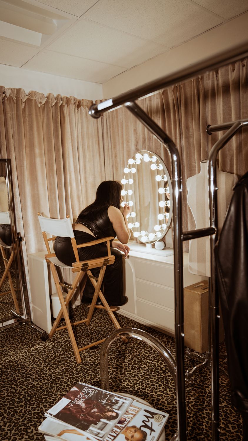 A lit vanity mirror with round bulbs in a dressing room, a director's chair beside it
