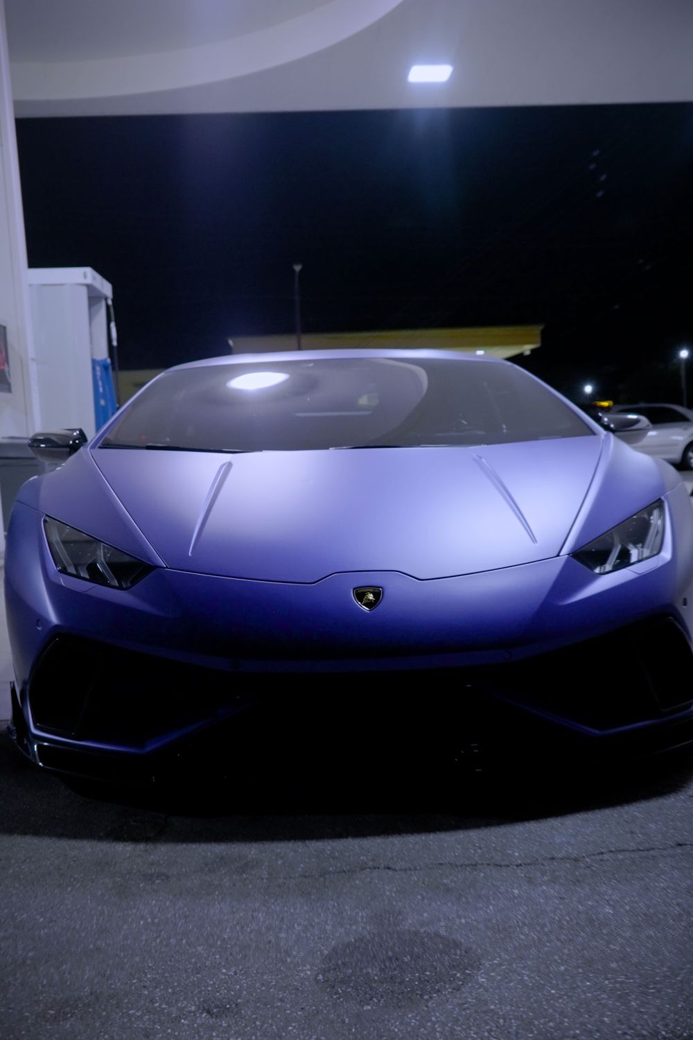Purple Lamborghini sports car seen head-on under the lights of a night gas station