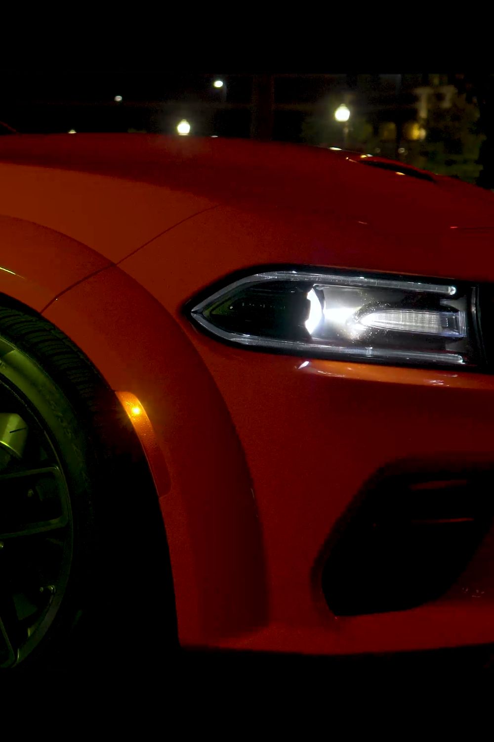 Red muscle car at night: front fender, wheel and LED headlight