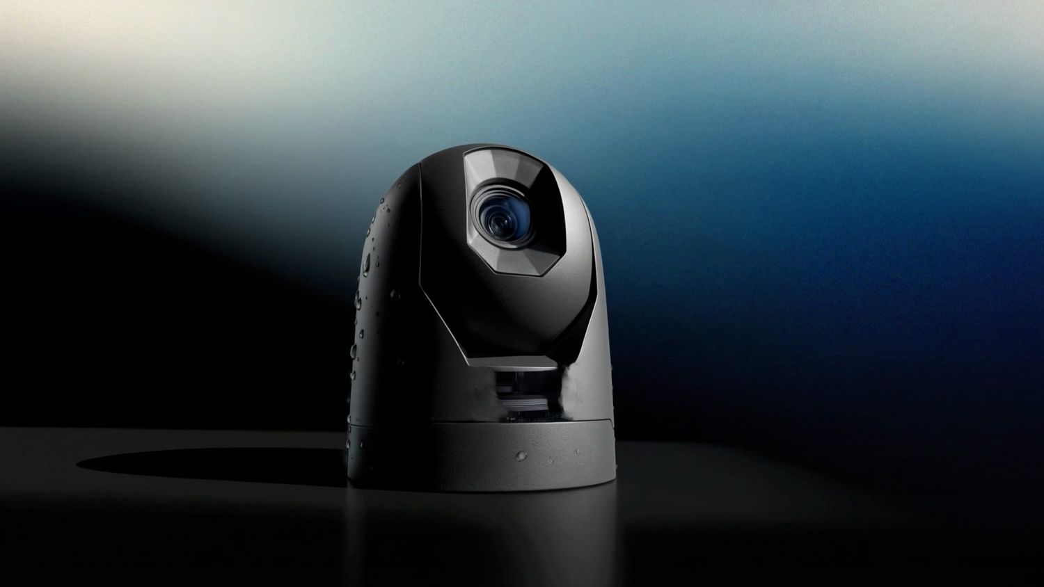 A matte-black marine camera dome beaded with water droplets on a reflective surface against a deep blue gradient