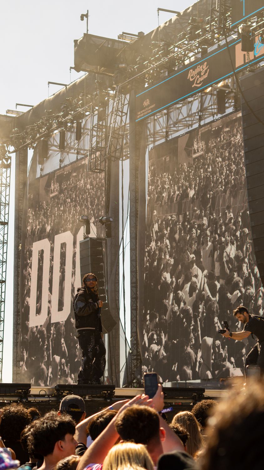 Black-and-white festival crowd beneath towering stage screens, a performer small on the stage below