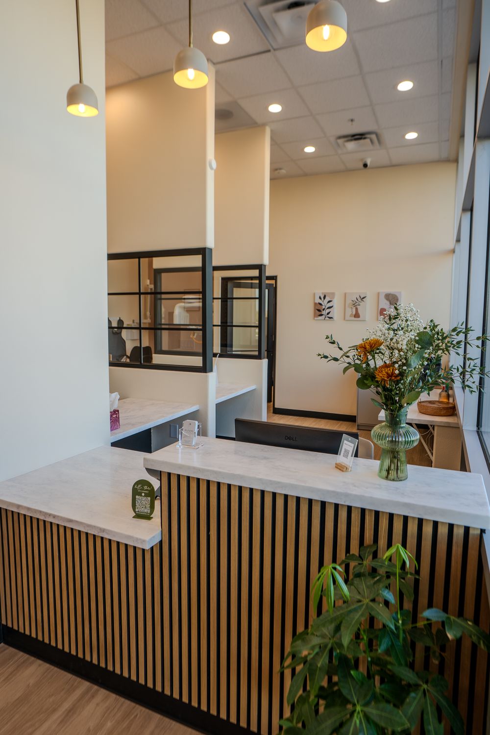 A reception counter faced in vertical wood slats, a vase of orange flowers on top and pendant lamps overhead