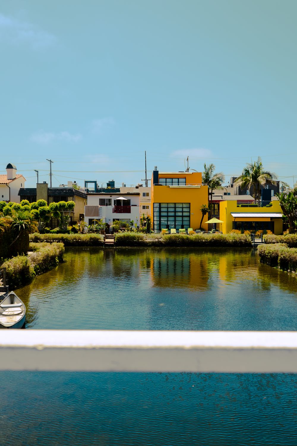A still canal in Venice, California, with colorful modern homes along the far bank under a clear sky